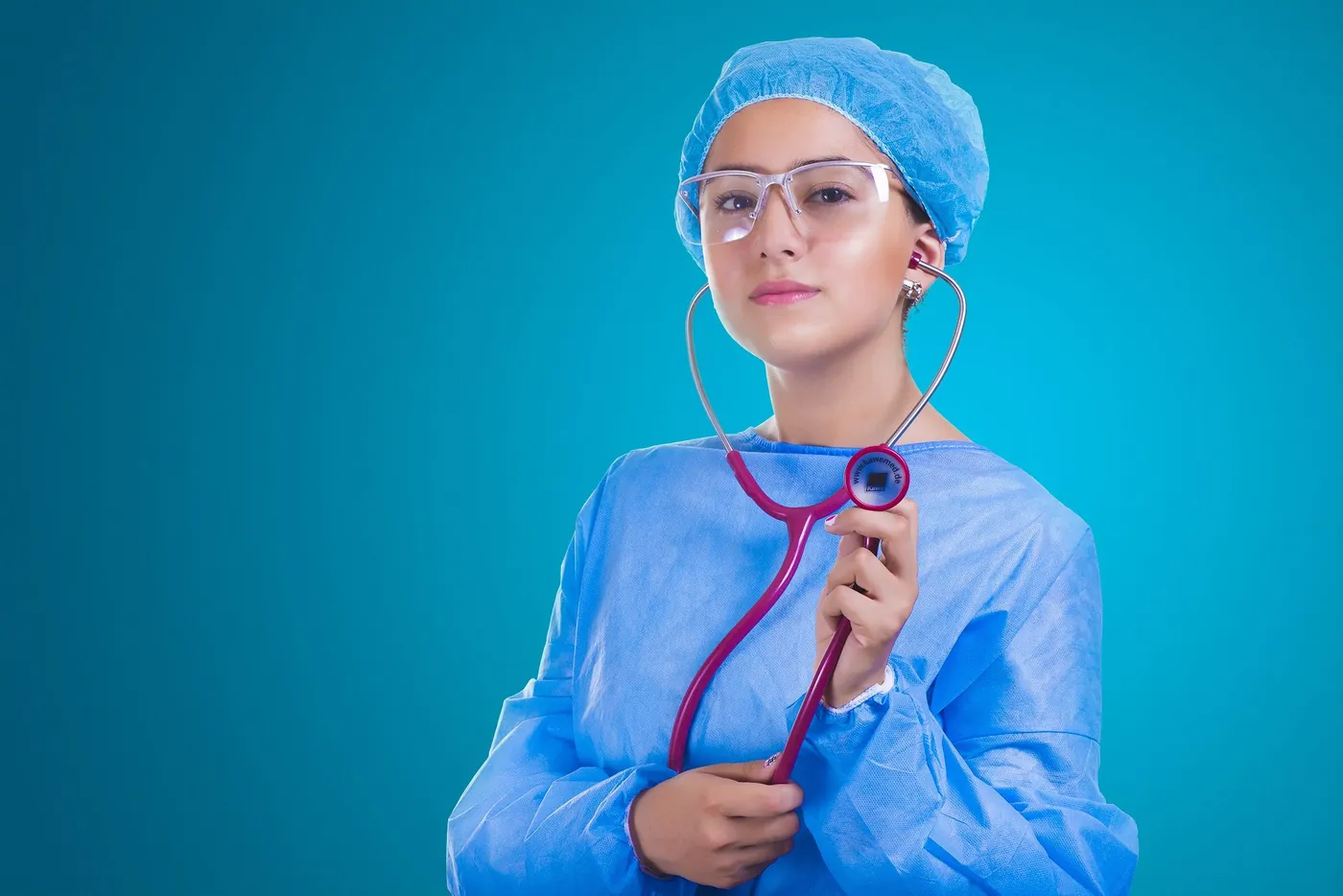 Een zorgmedewerker in lichtblauw uniform en een witte jas, met een stethoscoop, loopt over een gang. Stockfoto, geen opdrachtgever van Arbopartner Brabant.